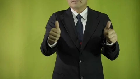 A man in a suit, on a green background, in the foreground, shows his thumbs up. Stock-Footage 275348465