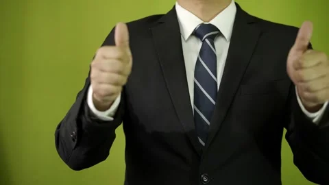 A man in a suit, on a green background, in the foreground, shows his thumbs up. Video stock 275349981