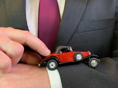A man in a suit holds a toy car in his hands. Businessman points a finger at  Stock Photos