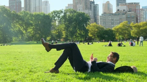 A man in a suit lies on the grass in central park in new york with a phone Stock Footage 277123307
