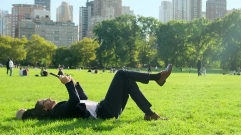 A man in a suit lies on the grass in central park in new york with a phone Stock Footage 277306050