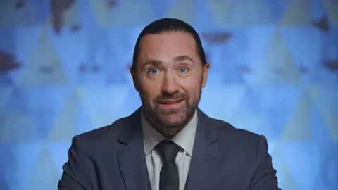 A man in a suit looking at the camera, telling the news, the host of the program Stock Footage 233717715