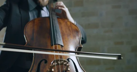 A man in a suit playing a cello in a dark room with brick walls Stock Footage 87223443