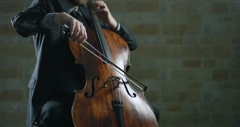 A man in a suit playing a cello in a dark room with brick walls Stock Footage 87223455