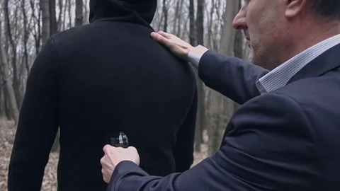 A man in suit points the gun to another man's back Stock Footage 105559734