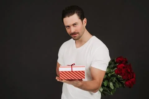 Man in suit is posing on black background with gift box and red roses in hands Stock Photos
