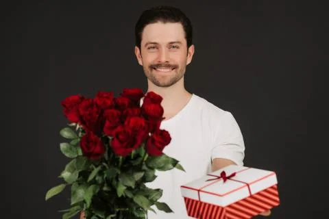 Man in suit is posing on black background with gift box and red roses in hands Stock Photos
