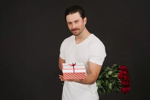 Man in suit is posing on black background with gift box and red roses in hands Foto stock