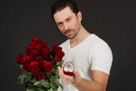 Man in suit is posing on black background with ring and red roses in hands. Stock Photos