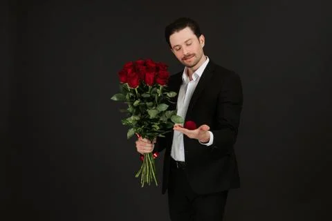 Man in suit is posing on black background with ring and red roses in hands. Stock Photos