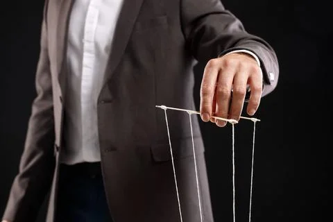 Man in suit pulling strings of puppet on black background, closeup Stock Photos