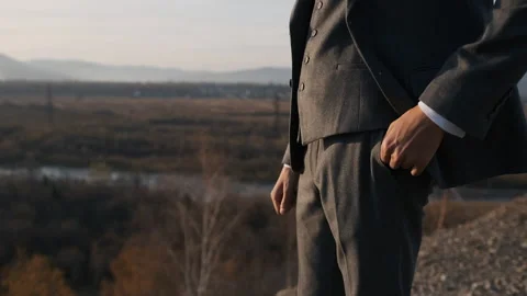 A man in a suit puts his hand in his pocket on the edge of the cliff Stock Footage 179939622