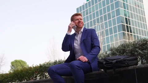 A man in a suit is sitting on a bench and talking on his cell phone Stock Footage 278645205