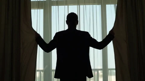 Man in suit stand against large window, stretch out hands and shut curtains Stock Footage 80741517