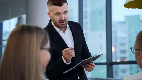 Man in suit standing in front of his colleagues holding a folder and a pen. Stock Footage 168528486