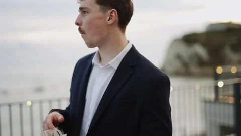 A man in a suit is standing on a pier overlooking the ocean Stock Footage 295995881
