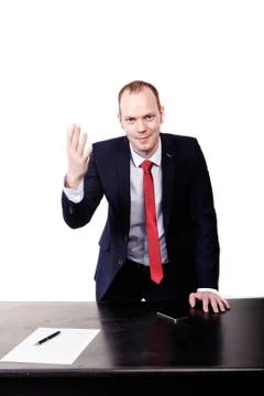 A man in a suit is standing at a table with a raised hand, on the table an Foto stock