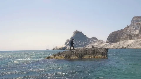 Man in suit stranded on a deserted rock in the middle of the ocean talking on 스톡 동영상 77780801