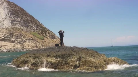 Man in suit stranded on a deserted rock in the middle of the ocean looking Stock Footage 77815285