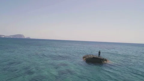 Man in suit stranded on a deserted rock in the middle of the ocean Stock Footage 77916981
