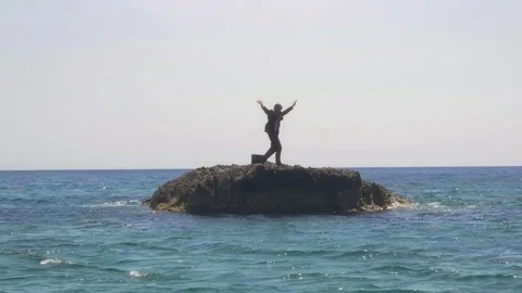 Man in suit stranded on a deserted rock in the middle of the ocean waving his Stock Footage 78016897