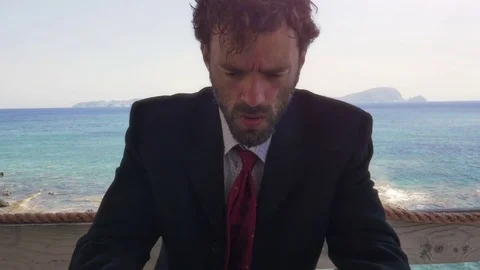 Man in suit talking on his smartphone on a balcony on an island in front of the Stock Footage 77678650