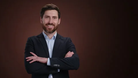 A man in a suit turning to the camera and crossing his arms with a smile Stock Footage 237558178