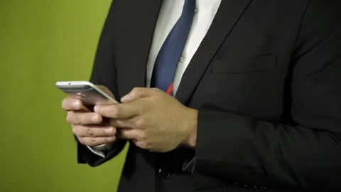 Man in suit typing and scrolling on his cell phone on green background  Video stock 275351287