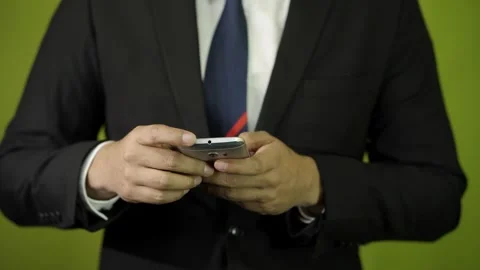 Man in suit typing and scrolling on his cell phone on green background  Stock Footage 275351388