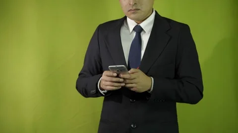 Man in suit typing and scrolling on his cell phone on green background  Video stock 275352863