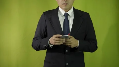 Man in suit typing and scrolling on his cell phone on green background  Video stock 275352951