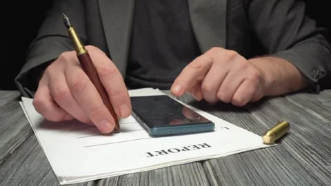 Man in suit using smartphone while writing on a report document with a fountain Stock Footage 327721127
