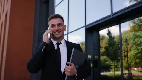 A man in a suit is walking and talking on his smartphone while holding a laptop Stock Footage 280612489