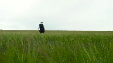 Man in suit walking ghrough the green field Stock Footage 64915732