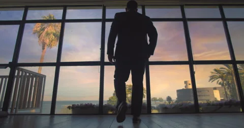 Man in suit walking towards the big window at sunset, looking at the lake, ch Stock Footage 146200581