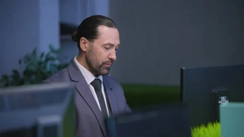 A man in a suit works at a computer in an empty office Stock Footage 233716914