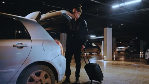 Man with suitcase loading car trunk in underground parking garage Vídeos de archivo 335474833