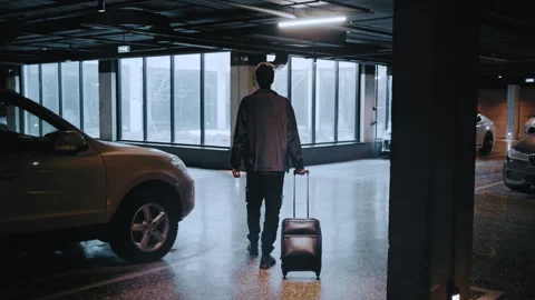 Man with a suitcase walking in underground parking garage 스톡 동영상 335474698