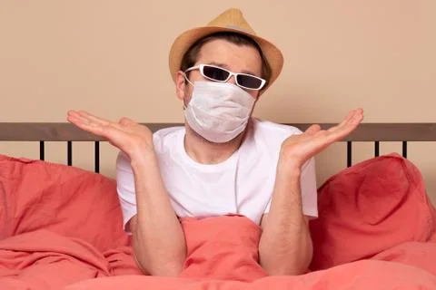 Man in summer hat and glasses in bed wearing mask protection mask. Stay home Stock Photos