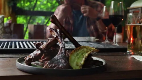 A man in a summer kitchen sitting at a table drinking beer and eating grilled me Stock Footage 280196822