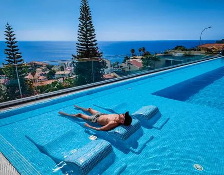 A man with a sun hat lying on a sunbed in a water in a panoramic pool Stock Photos