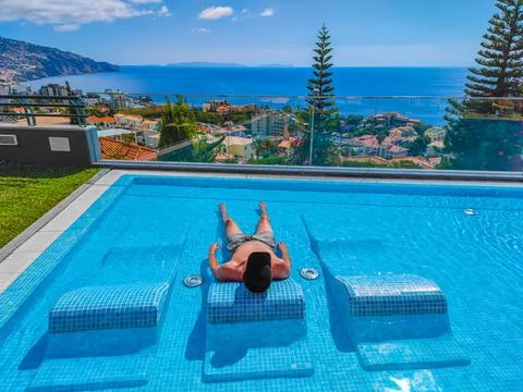 A man with a sun hat lying on a sunbed in a water in a panoramic pool Stock-Fotos
