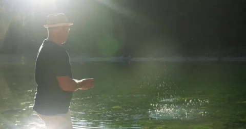 A man in the sun throws stones on the water on the lake. Rear view Stock Footage 246491676