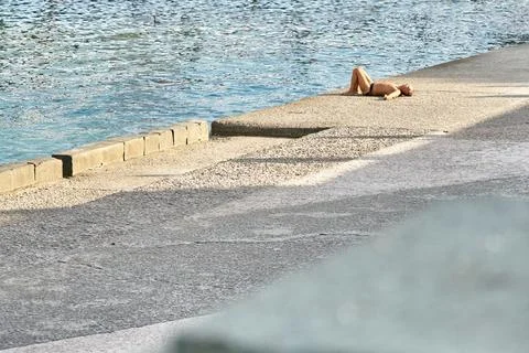 Man sunbathes lying on empty stone embankment near sea Foto stock