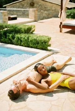 Man sunbathes lying by the pool hugging woman who rests her head on his stomach Foto stock