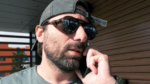 A man with sunglasses and a baseball cap talks on the phone on a sunny day 库存影片 277857404