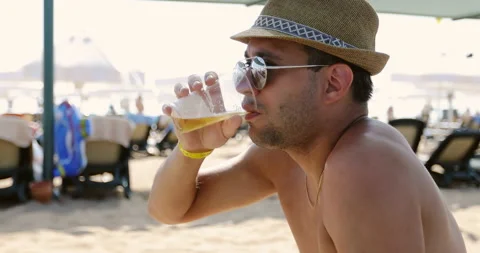 A man in sunglasses and a hat drinks beer on the beach. Stock Footage 140156738