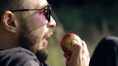 Man in sunglasses eats an apple on nature Video stock 96218831