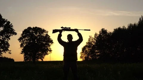 Man on a sunset background holds a gun over his head Stock Footage 80325306