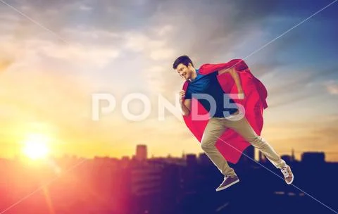 Man in superhero cape flying over sunset in city Stock Photos